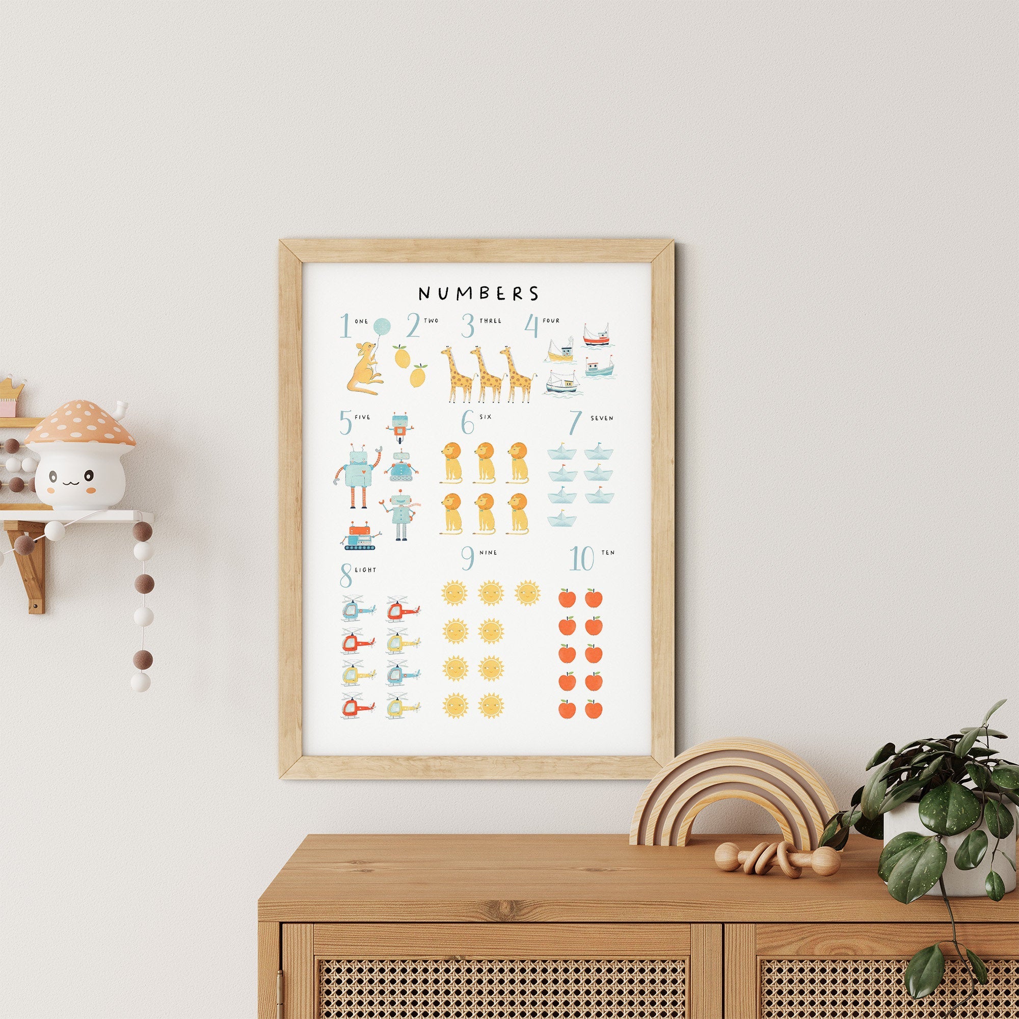 The Numbers & Alphabet Nursery Print by My Store is a framed poster with numbers 1 to 10 and cute animal illustrations, adding educational value. To its left, a small shelf holds a toy, while below is a wooden cabinet with a potted plant—ideal nursery art for any childs room.