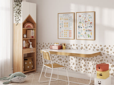 A cozy childrens room includes a wooden desk and chair, a house-shaped bookshelf, and My Stores Numbers & Alphabet Nursery Print on the wall. The space comes alive with a green plush whale toy and colorful storage boxes, adding playful elements to this enchanting environment.
