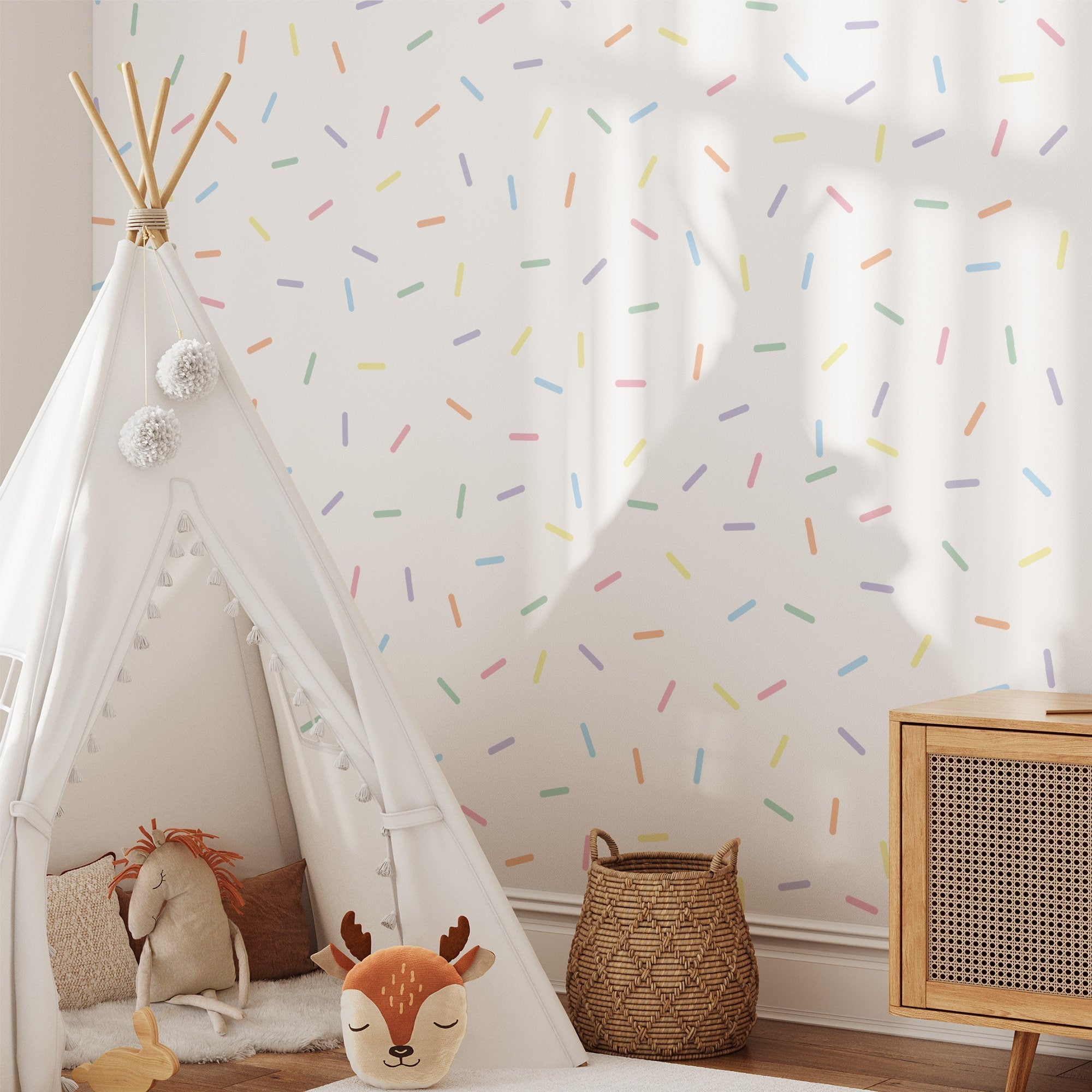 A cozy childrens room features a white play tent with a furry animal pillow inside. The wall is adorned with My Stores Pastel Sprinkle Stickers, and a wicker basket sits by a wooden cabinet on the right, adding charming nursery decor touches.