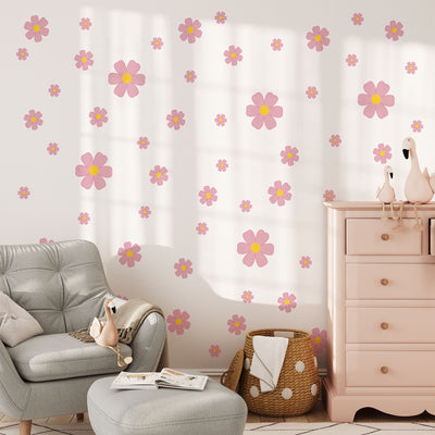 A cozy nursery features a light gray armchair, pink dresser, stuffed animals, and walls adorned with Pink Daisy Floral Wall Decals by My Store. A basket with a blanket sits on the floor to complete the inviting look.