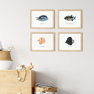A nursery features four Reef Fish Nursery Print illustrations from My Store labeled Blue Tang, Clown Triggerfish, Copperband, and Gem Tang on a beige wall. Below, a wooden cabinet with a basket, toy, and heart-patterned cloth adds educational fun to the decor.