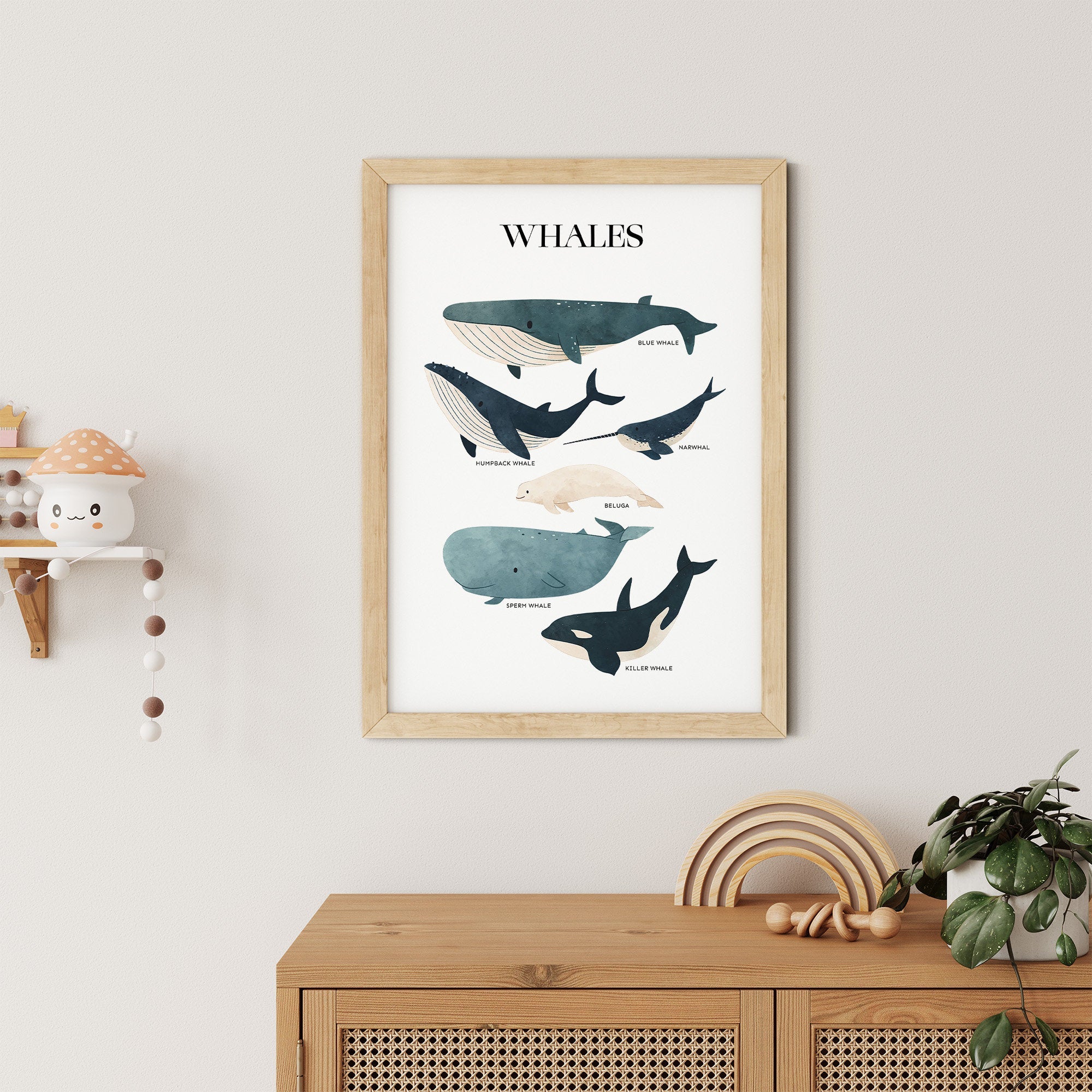 A framed Whales poster by My Store, showcasing various whale illustrations, is ideal for an ocean-themed nursery. Below, a wooden cabinet and a shelf displaying a mushroom figure enhance the charm of this Sea Animals Nursery Print setup.